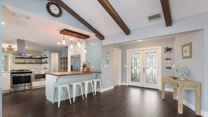 A spacious kitchen with dark wooden floors, a central island with stools, a dining area with a wooden table, and a large window. - House has power ,Fast WIFI，Near Anna Maria beach (Bradenton)