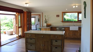 A spacious kitchen with wooden cabinets, a large island, and a view of greenery outside. - Large Country Home with Views - Spa Pool, Swimming Pool, Firepit, Games Room (Redwood Valley)