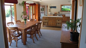 A spacious dining area with a wooden table and chairs, a potted plant, and a view of the garden through large windows. - Large Country Home with Views - Spa Pool, Swimming Pool, Firepit, Games Room (Redwood Valley)