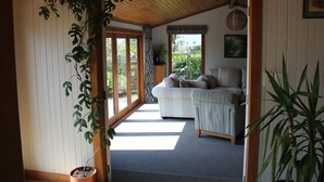 A room with a wooden ceiling, a sofa, a potted plant, and a view of the outdoors. - Large Country Home with Views - Spa Pool, Swimming Pool, Firepit, Games Room (Redwood Valley)