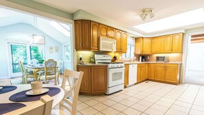 A kitchen with wooden cabinets, a stove, and a microwave. There is a dining table with chairs and a window providing natural light. - Spacious Home w/ Fire Pit and Central AC! (Eastham)