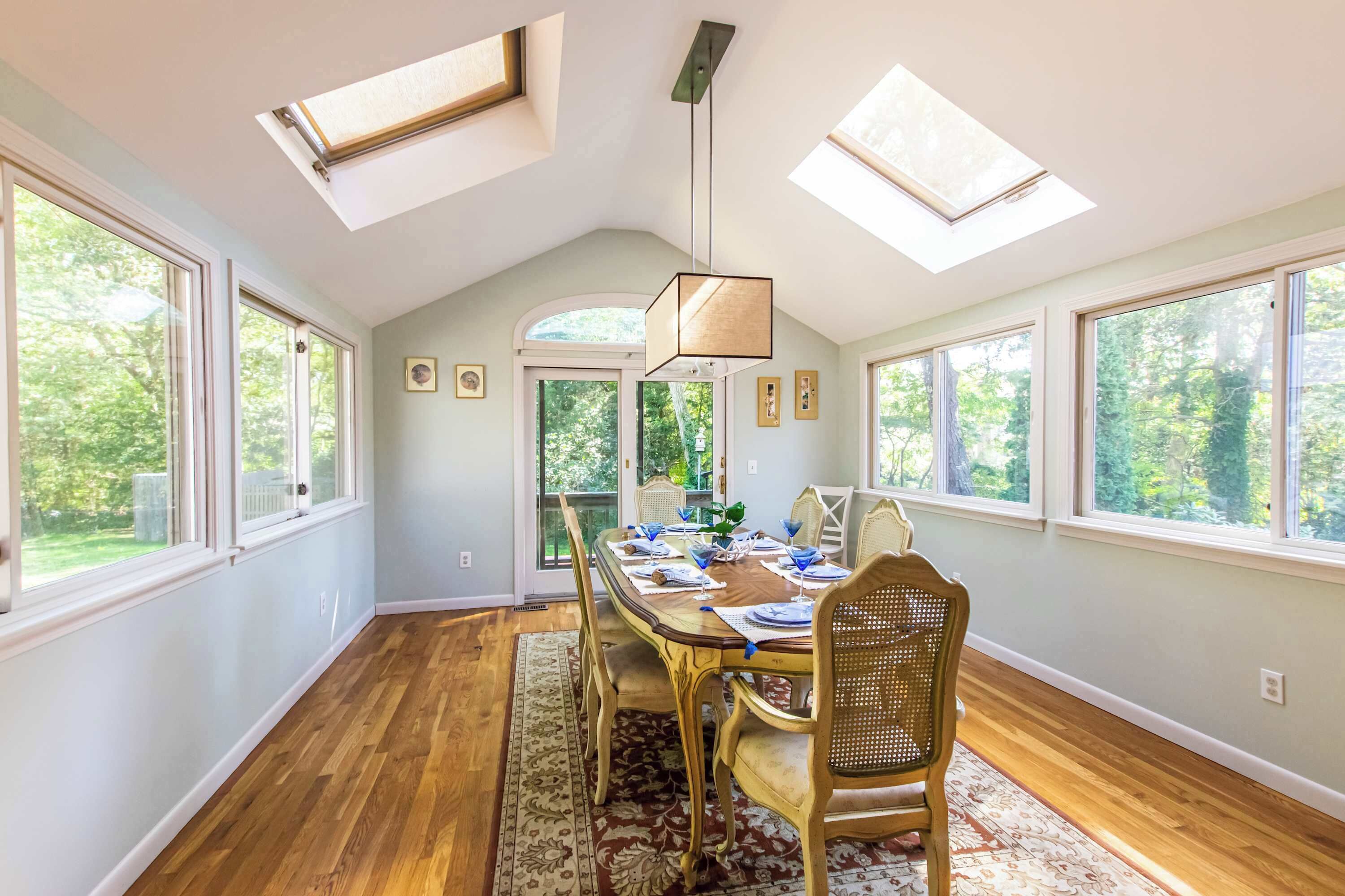 A dining room with a large table, chairs, and a chandelier. There are skylights and large windows providing natural light.