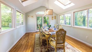 A dining room with a large table, chairs, and a chandelier. There are skylights and large windows providing natural light. - Spacious Home w/ Fire Pit and Central AC! (Eastham)