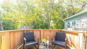 A wooden deck with two wicker chairs and a small table, surrounded by a wooden fence, with trees in the background. - 100 Ft to Skaket Beach! (Orleans)