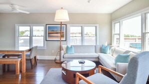 A living room with a sofa, a round coffee table, a dining table with chairs, and a floor lamp. - Renovated Oceanfront Penthouse! (Provincetown)