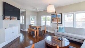 A living room with a flat-screen TV, a dining table, a sofa, and a lamp. - Renovated Oceanfront Penthouse! (Provincetown)