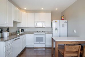 Una cocina con armarios blancos, estufa, microondas y refrigerador.