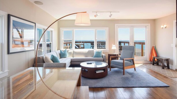A modern living room with a sofa, armchair, coffee table, and a view of the sea through large windows. - Renovated Oceanfront Penthouse! (Provincetown)