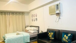 Una habitación con una cama, un sofá negro, un aire acondicionado y una lámpara en el techo.