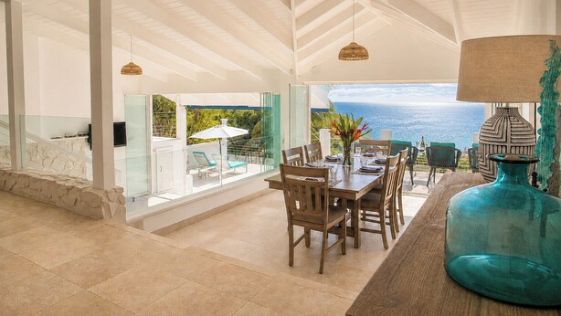 Un'ampia sala da pranzo con vista sull'oceano, una parete in pietra e un grande vaso blu.