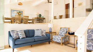 Un soggiorno con un divano blu, cuscini decorati, una sedia di legno, un tavolino con una lampada e una scala con piastrelle decorate.