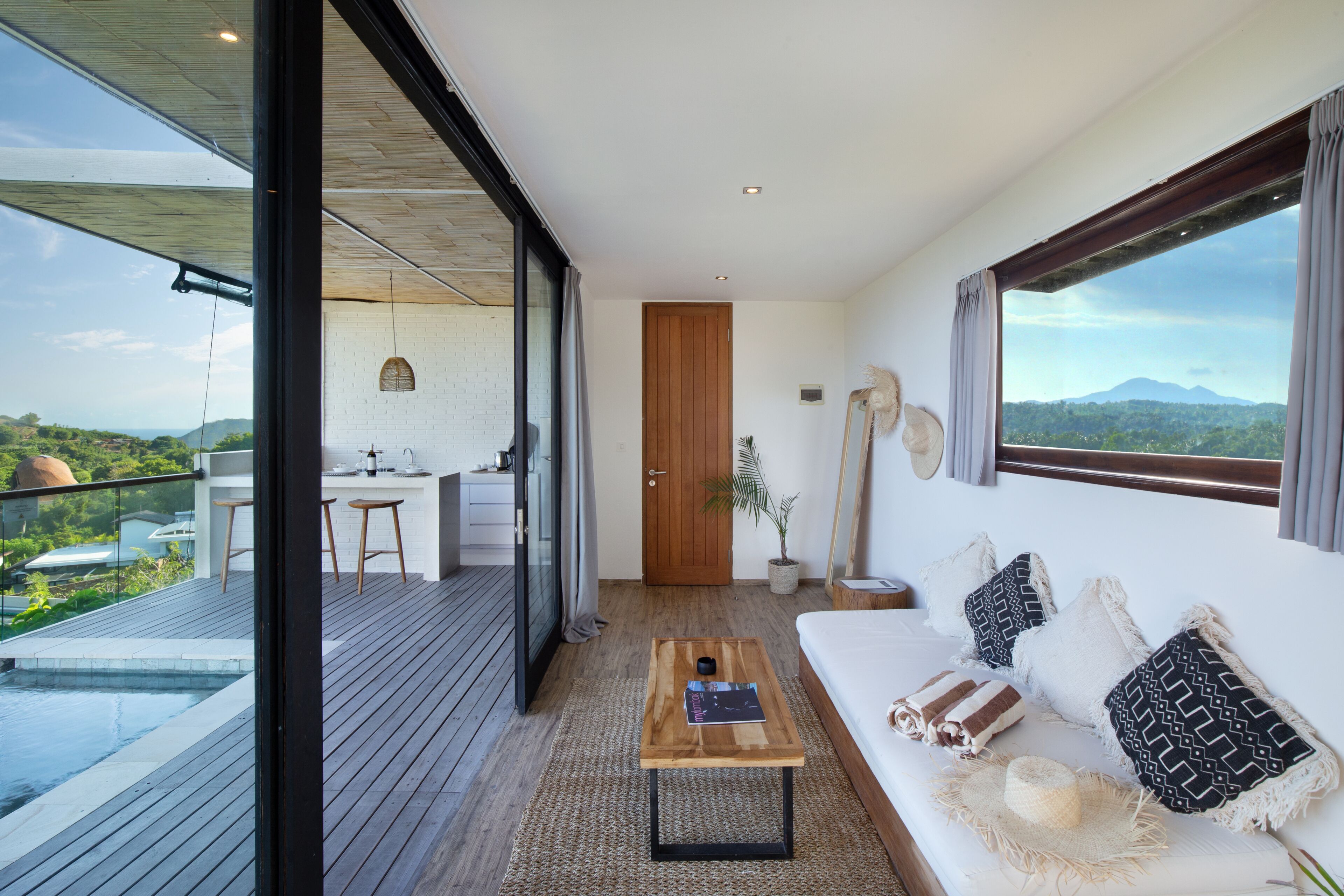 Ein modernes Hotelzimmer mit Holzbalkon, einer Couch mit gemusterten Kissen, einem Couchtisch und Blick auf die Berge.