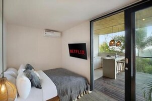 Un dormitorio moderno con cama, televisor montado en la pared y balcón con vistas.