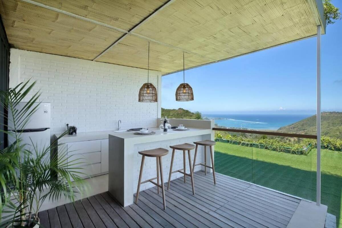 Una cocina con salpicadero de ladrillo blanco, taburetes de bar de madera, lámparas colgantes y vista al océano.