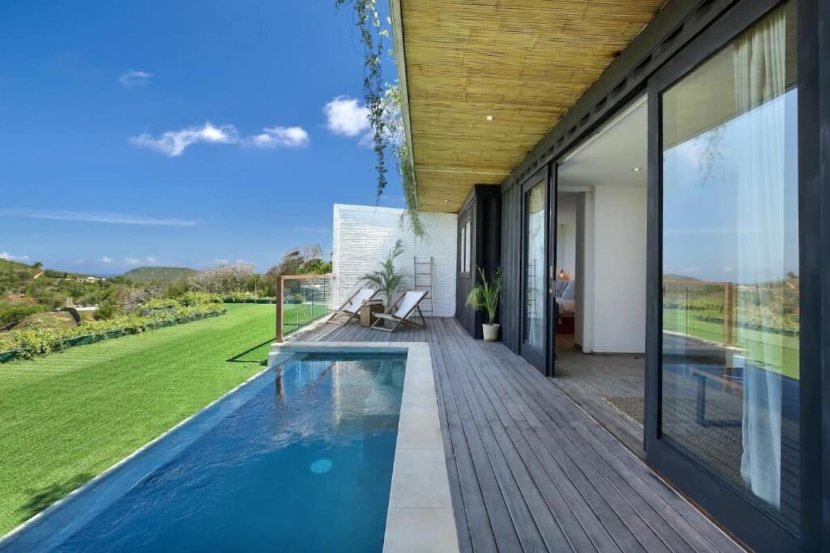 Un área de piscina moderna al aire libre con cubierta de madera, sillas de descanso y vistas del paisaje circundante.