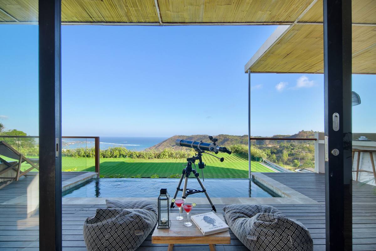 Un telescopio en una terraza con vista a una piscina y al océano.