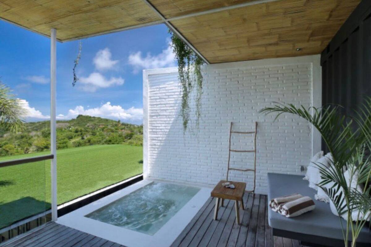 Zona de spa con jacuzzi, terraza de madera, pared de ladrillo blanco y vistas al exterior.
