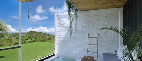 Zona de spa con jacuzzi, terraza de madera, pared de ladrillo blanco y vistas al exterior.