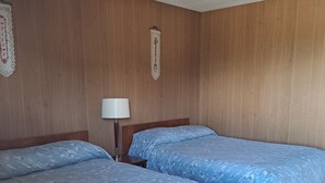 A hotel room with two beds, a red carpet, wooden panel walls, a white ceiling, and a wall-mounted lamp.