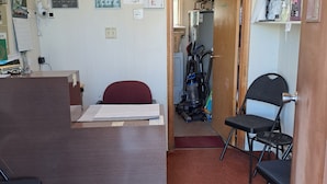 A small office with a desk, chairs, a welcome sign, and a door leading to a storage area.