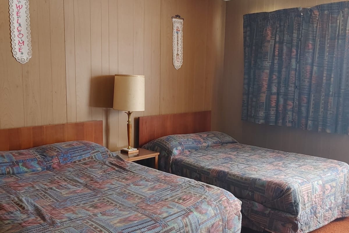 Una habitación de hotel con dos camas, un cabecero de madera, una lámpara y una cortina.