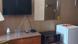 A hotel room with a wooden paneled wall, a flat-screen TV mounted above a wooden desk, a microwave, a mini-fridge, and a cabinet with a decorative panel.