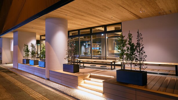 An outdoor area with wooden benches, planters with trees, and a staircase leading to an upper level. - MURE Beppu (Beppu)