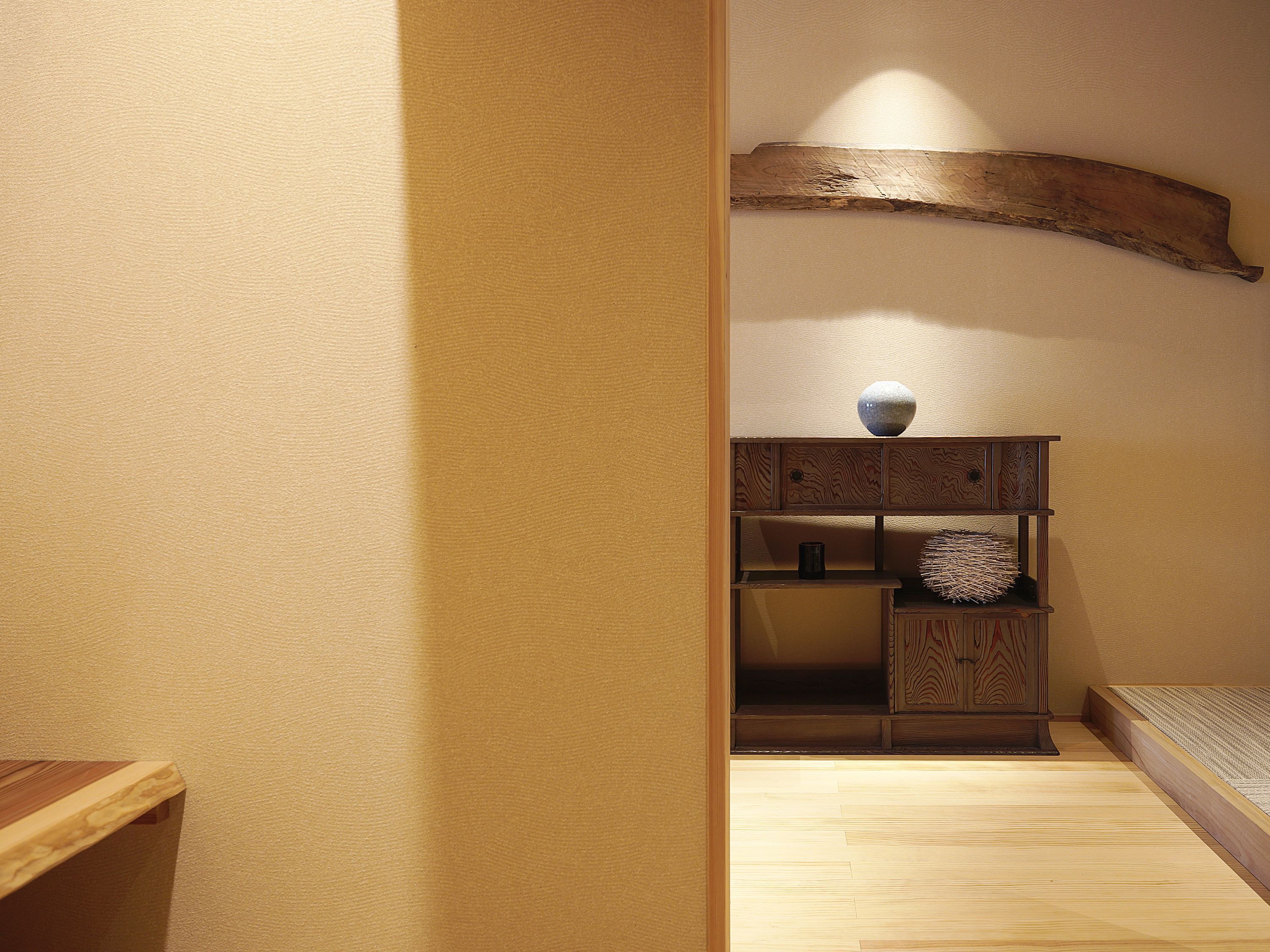 A room with a wooden bench, a small cabinet with decorative items, and a sloped ceiling.