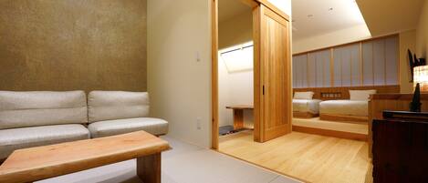 Een moderne hotelkamer met een bank, een houten zitbank, een bed en een schuifdeur naar een badkamer.