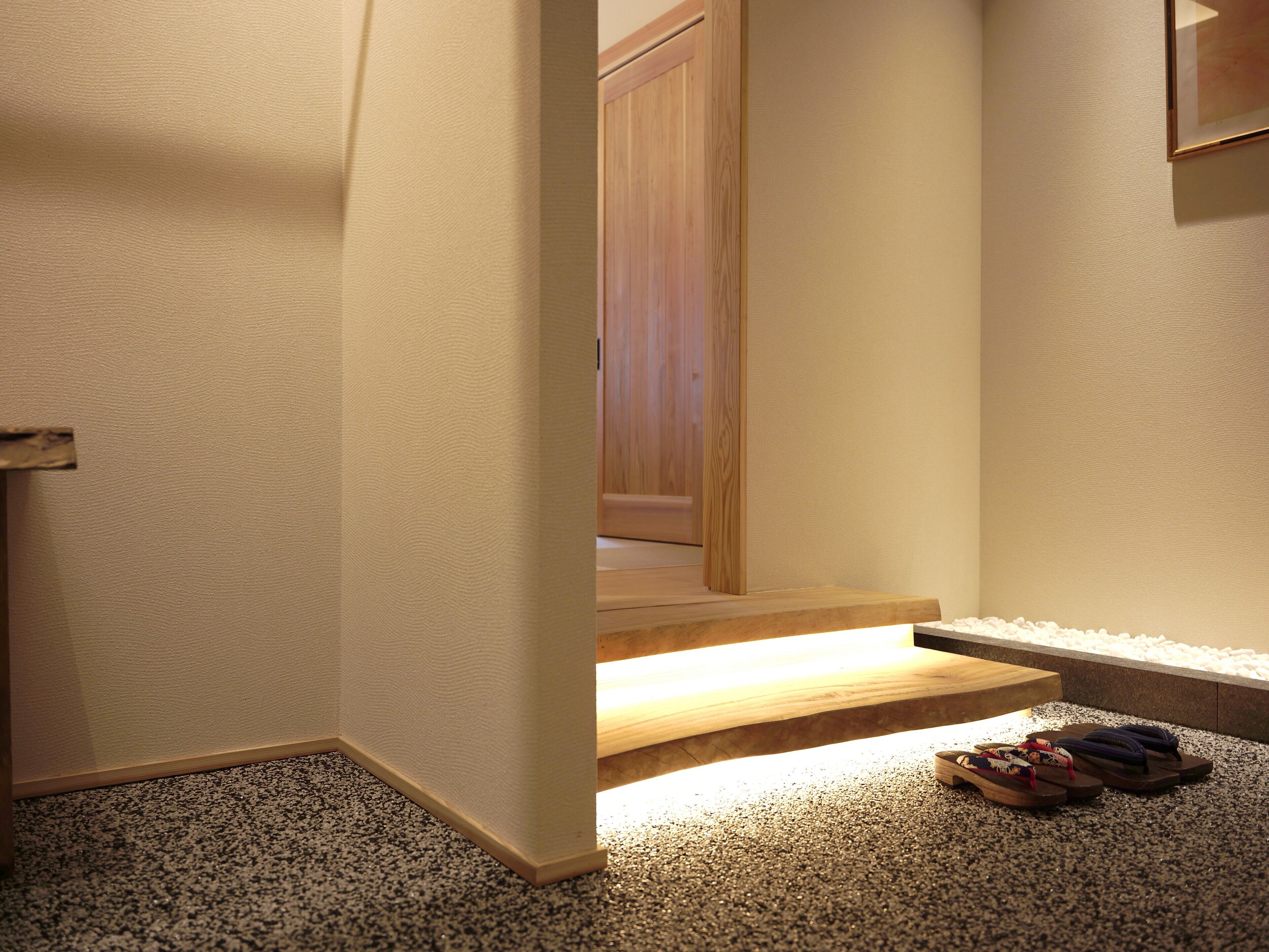 A hallway with a carpeted floor, wooden steps leading to a door, and a pair of flip-flops on the right.