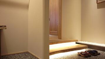 A hallway with a carpeted floor, wooden steps leading to a door, and a pair of flip-flops on the right.