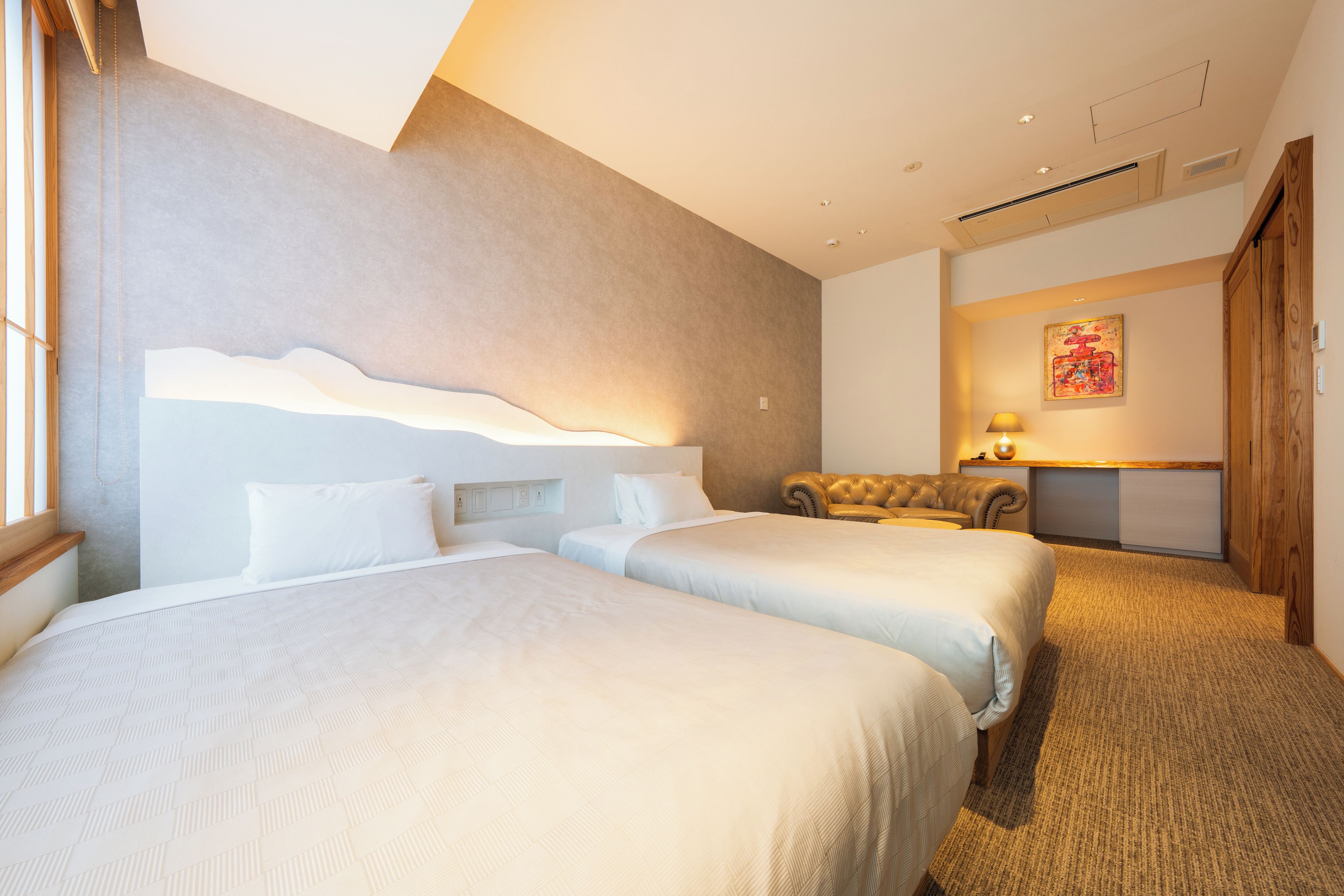 Ett hotellrum med två sängar, en soffa, en lampa och en tavla på väggen.