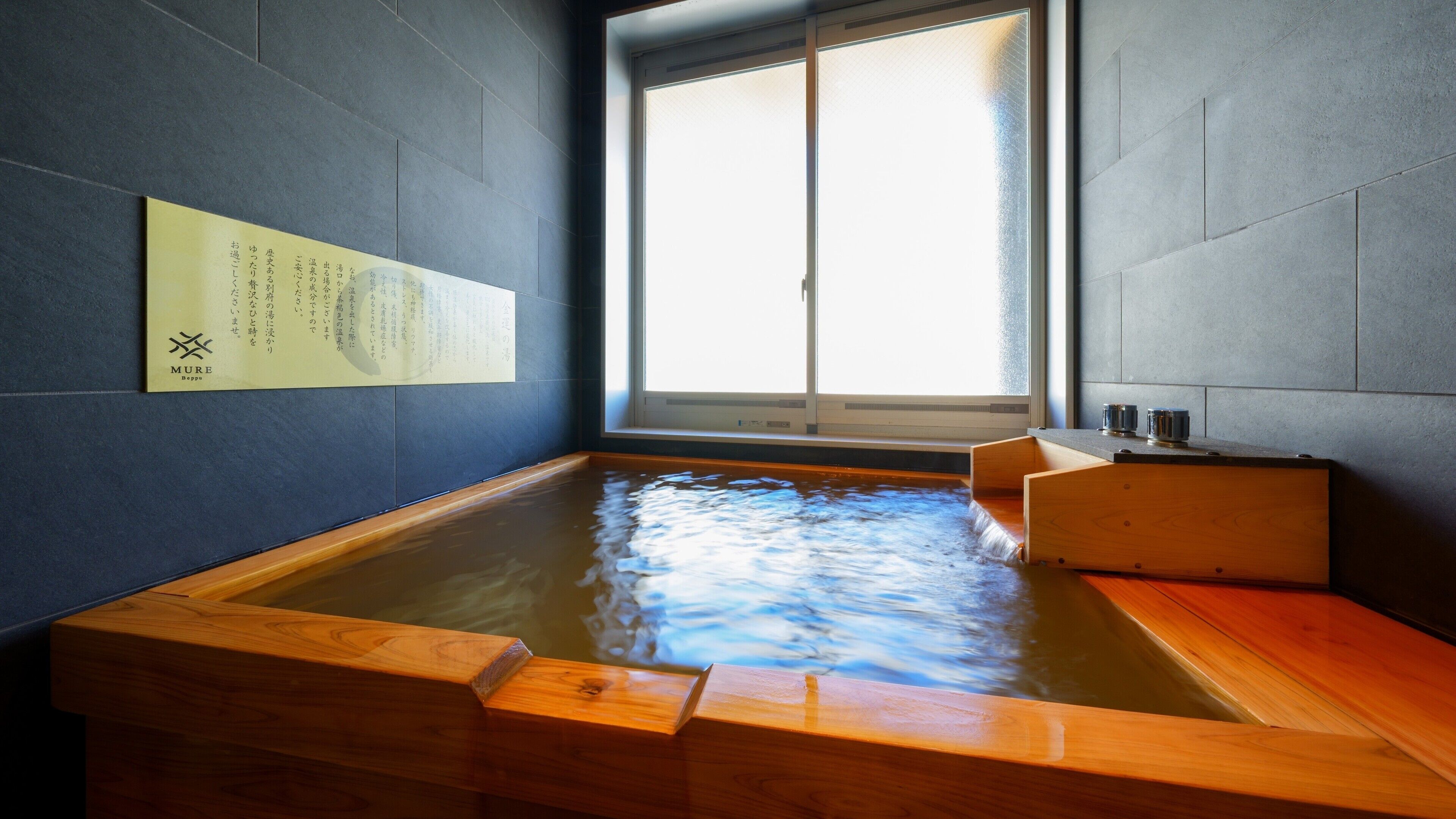 A traditional Japanese onsen with a wooden bath, a sliding glass door, and a sign with Japanese text.