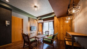 Quarto com piso de madeira, mesa de jantar com cadeiras, TV fixada na parede e janela com cortinas.