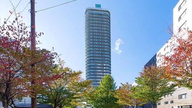 Um edifício moderno de arranha-céus com fachada curva, rodeado por árvores em tons de outono e um canal.
