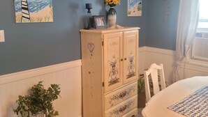 Un dormitorio con una cama, un aparador con motivos florales, una planta en maceta y dos cuadros en la pared.