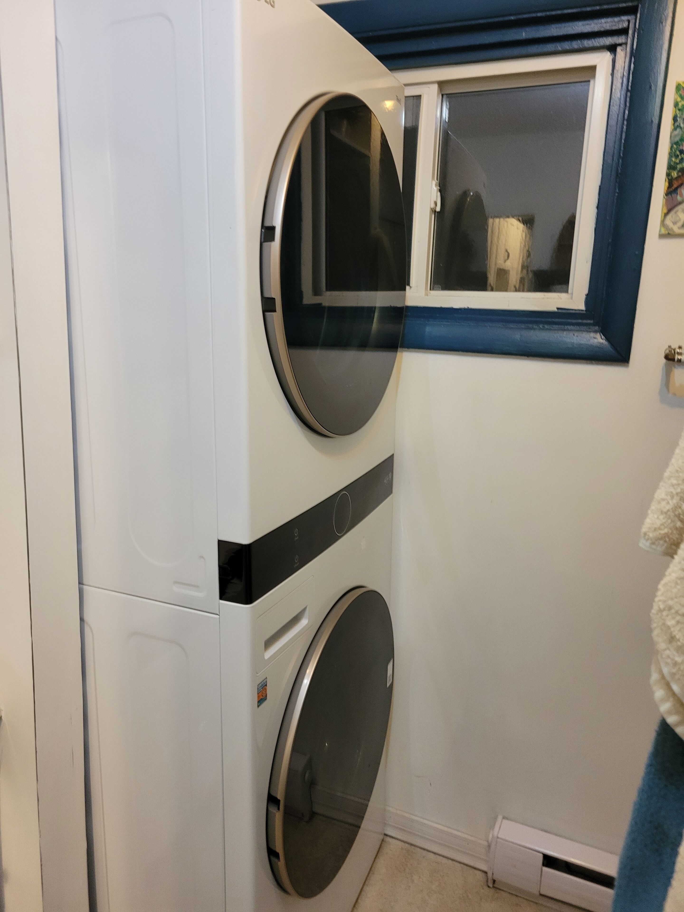 Une petite buanderie équipée de deux machines à laver, d’une petite fenêtre et d’une serviette accrochée au mur.