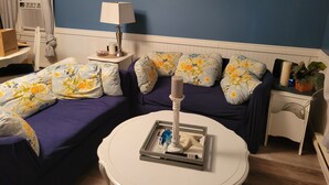 Un salón con pared azul, dos sofás con cojines florales, una mesa de centro redonda, una lámpara y dos cuadros de paisajes marinos.