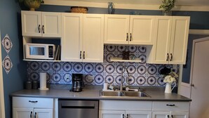 Una cocina con armarios blancos, lavavajillas de acero inoxidable, cafetera y fregadero.