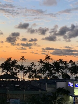 Une vue au coucher du soleil, avec des palmiers et un bâtiment sur lequel on peut lire l’inscription « KANADU ».