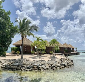 A beachfront resort with thatched-roof huts, palm trees, and a rocky shoreline. - Oceanside Luxury @ The Cove Palm Beach 2BR 2.5BA (Palm Beach)