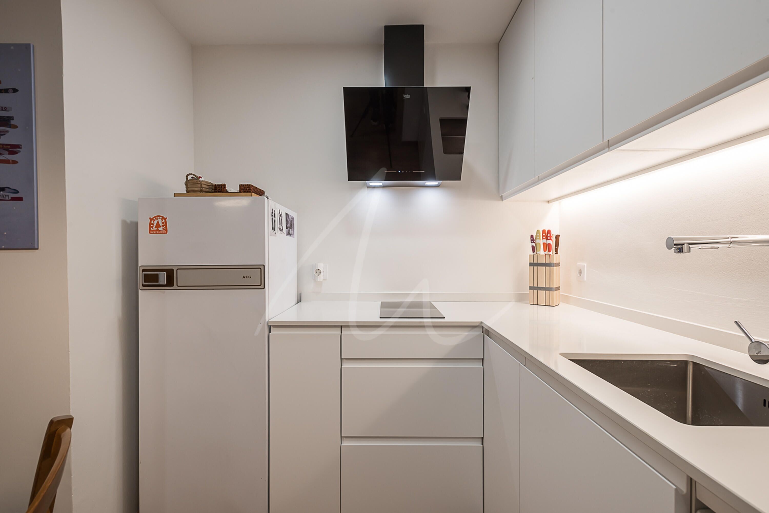 A modern kitchen with white cabinetry, a built-in oven, and a stainless steel sink.