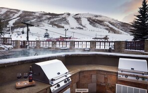 Un espace extérieur avec piscine, un barbecue en pierre et une vue sur une station de ski en arrière-plan.