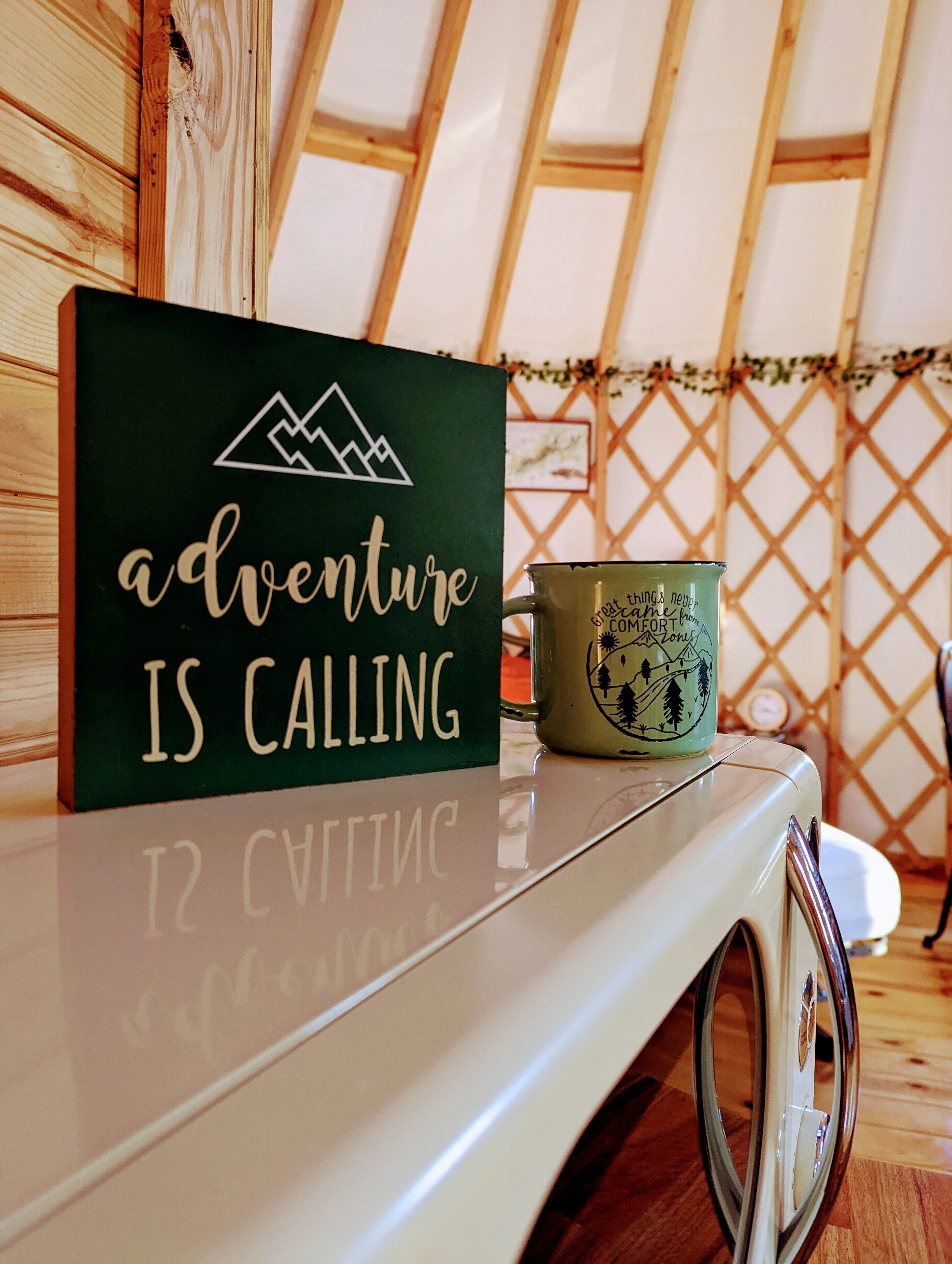 A sign with the text "adventure is calling" and a mug with a mountain design.