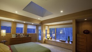 A bedroom with a large bed, built-in storage, a skylight, and windows with blinds. - Mid-Century Modern Retreat on Private 10 Acres with 1-Acre Pond & Nature Trails. (Midland)