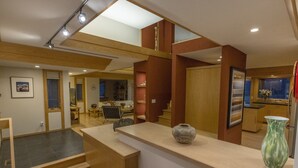 A modern interior with a staircase leading to a second floor, a kitchen area with wooden cabinets, and a dining space with a table and chairs. - Mid-Century Modern Retreat on Private 10 Acres with 1-Acre Pond & Nature Trails. (Midland)