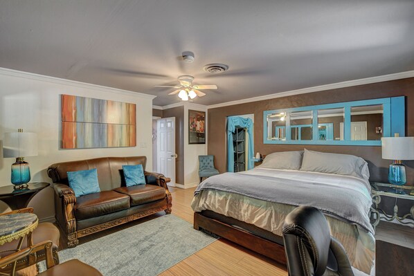 A bedroom with a large bed, a brown leather sofa, a small table, and a chair.