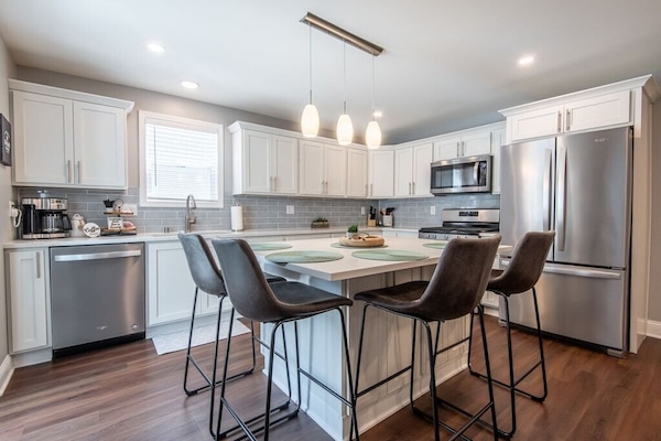 Lower kitchen island with 4 chairs around island and stainless steel appliances