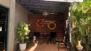 Un espace extérieur aménagé en patio, avec un mur en bois, deux bouées de sauvetage, une table, des chaises et des plantes en pot.
