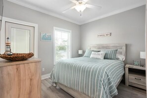 A bedroom with a bed, a nightstand, a wall-mounted shelf, a window with blinds, and a ceiling fan.